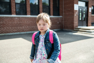 A portrait of trisomie 21 child girl outside on a school playground