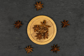 Lot of whole dry brown star anise illicium verum on round bamboo coaster flatlay on grey stone