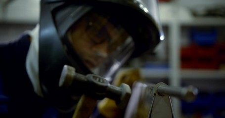 Close-up portrait of a welding master man in gloves and a helmet working with a part, knocking on it with a hammer, collects it.