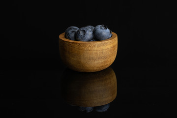Lot of whole fresh blue bilberry in tiny wooden bowl isolated on black glass