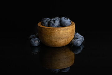 Lot of whole fresh blue bilberry in tiny wooden bowl isolated on black glass