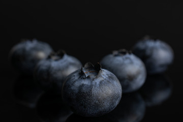 Group of five whole fresh blue bilberry isolated on black glass