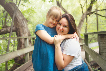 A portrait of trisomie 21 child girl outside with his mother