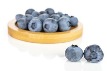 Lot of whole fresh blue bilberry on round bamboo coaster isolated on white background