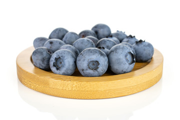 Lot of whole fresh blue bilberry on round bamboo coaster isolated on white background