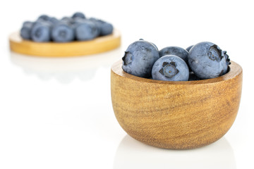 Lot of whole fresh blue bilberry in tiny wooden bowl on round bamboo coaster isolated on white background