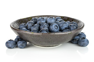 Lot of whole fresh blue bilberry in dark ceramic bowl isolated on white background