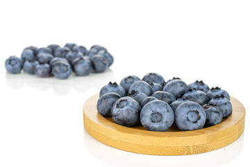 Lot of whole fresh blue bilberry on round bamboo coaster isolated on white background