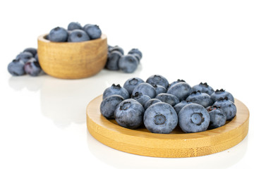 Lot of whole fresh blue bilberry in tiny wooden bowl on round bamboo coaster isolated on white background