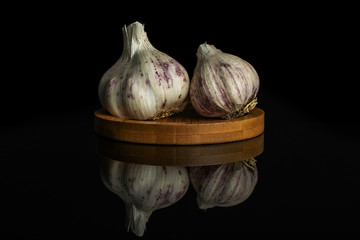 Group of two whole organic white garlic allium sativum on bamboo coaster isolated on black glass