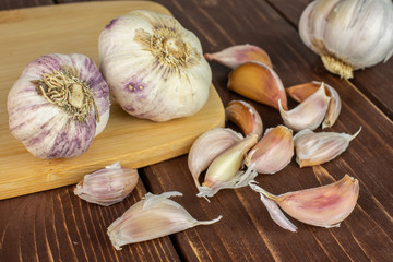 Group of three whole lot of pieces of organic white garlic allium sativum on bamboo cutting board on brown wood
