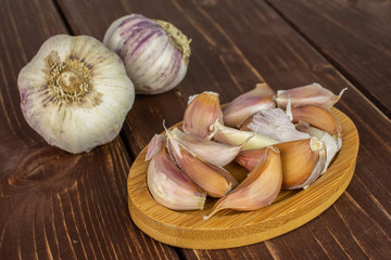 Group of two whole lot of pieces of organic white garlic allium sativum on bamboo coaster on brown wood