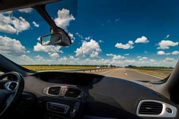 View of the road and landscape through the windshield of a passenger car, summer, noon, clouds in the sky