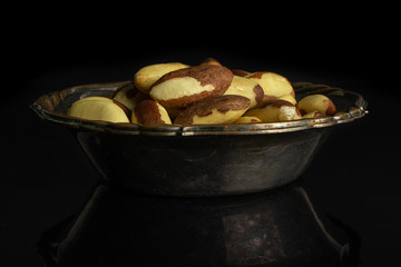 Lot of whole raw brown brazil nut in metal bowl isolated on black glass