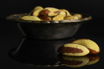 Lot of whole raw brown brazil nut in metal bowl isolated on black glass
