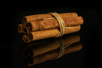 Group of six whole dry brown cinnamon wrapped in natural twine isolated on black glass © PIXbank