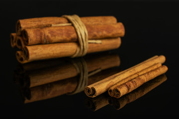 Group of eight whole dry brown cinnamon wrapped in natural twine isolated on black glass