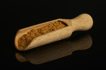 Dry brown cinnamon in a wooden scoop isolated on black glass