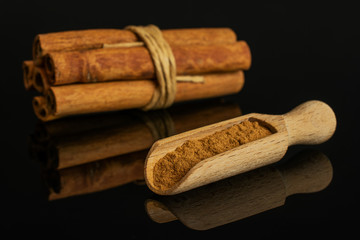 Group of six whole dry brown cinnamon wrapped in natural twine in a wooden scoop isolated on black glass