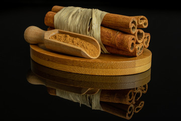 Group of six whole dry brown cinnamon wrapped in natural bast in a wooden scoop on oval bamboo...