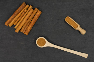 Lot of whole dry brown cinnamon in a wooden spoon in a wooden scoop flatlay on grey stone