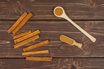 Lot of whole dry brown cinnamon in a wooden spoon in a wooden scoop flatlay on brown wood