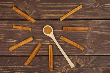Group of eight whole dry brown cinnamon in a wooden spoon flatlay on brown wood