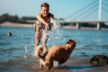 Woman playing with a dog in the river and splashing water