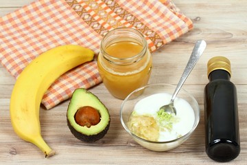 Ingredients for easy homemade facial mask...Banana, avocado, honey, olive oil, oatmeal and cream good for face mask, wood board