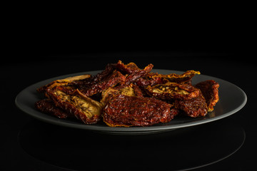 Lot of whole dried red tomato on gray ceramic plate isolated on black glass