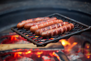 Forest Dinner tourist on grill. Delicious sausages are fried on fire in evening in the forest. dying embers of meat dinner traveler in forest