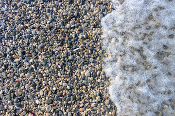 surf on the beach colored pebbles in the sea, top view, background