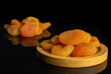 Lot of whole dried orange apricot on round bamboo coaster isolated on black glass