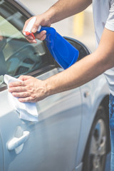Close up of man cleaning car with cloth and spray bottle, car maintenance concept.