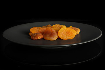 Lot of whole dried orange apricot on gray ceramic plate isolated on black glass