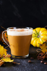 Pumpkin spiced latte or coffee in glass cup, dry leaves. Traditional autumn or winter hot drink.