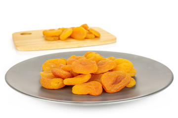 Lot of whole dried orange apricot on bamboo cutting board on gray ceramic plate isolated on white background