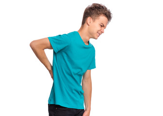 Portrait of unhappy teen boy suffering from backache, isolated on white background. Cute young teenager hands touching back pain. Upset child massaging his back suffering from discomfort ache pain. - 287763236