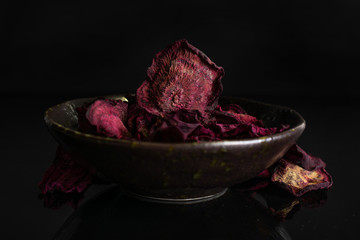 Obraz premium Lot of slices of dried red beetroot in dark ceramic bowl isolated on black glass