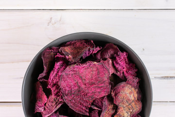 Lot of slices of dried red beetroot in gray ceramic bowl flatlay on white wood