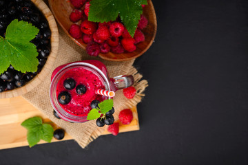 Raspberry and currant berry smoothie in a glass jar with a straw and mint leaf