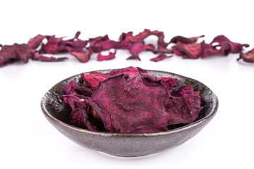 Lot of slices of dried red beetroot in dark ceramic bowl isolated on white background