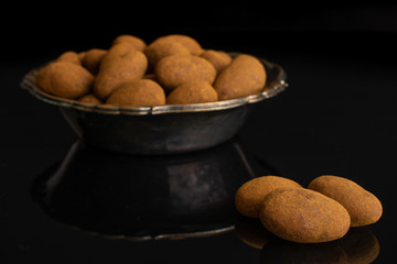 Lot of whole sweet brown chocolate cinnamon almond in metal bowl isolated on black glass