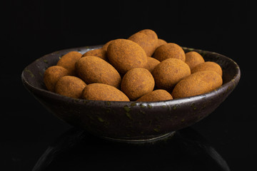 Lot of whole sweet brown chocolate cinnamon almond in dark ceramic bowl isolated on black glass