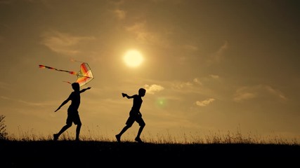 Happy family playing outdoors, flying kite flying. Silhouette of children with a kite at sunset. Team work, team play outdoor games