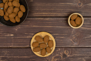 Lot of whole sweet brown chocolate cinnamon almond in tiny wooden bowl on round bamboo coaster in dark ceramic bowl flatlay on brown wood