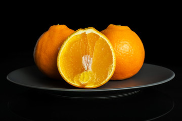 Group of two whole one half of fresh orange tangelo minneola on gray ceramic plate isolated on...