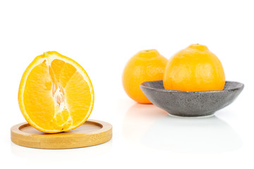 Group of two whole one half of fresh orange tangelo minneola in dark ceramic bowl on round bamboo coaster isolated on white background