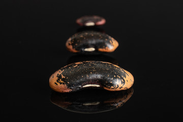 Group of three whole stained purple bean isolated on black glass