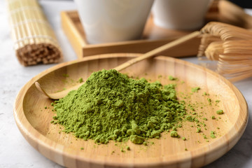 Matcha green tea powder on a wooden round plate,tawan, tasaku and a bamboo whisk on  concrete background